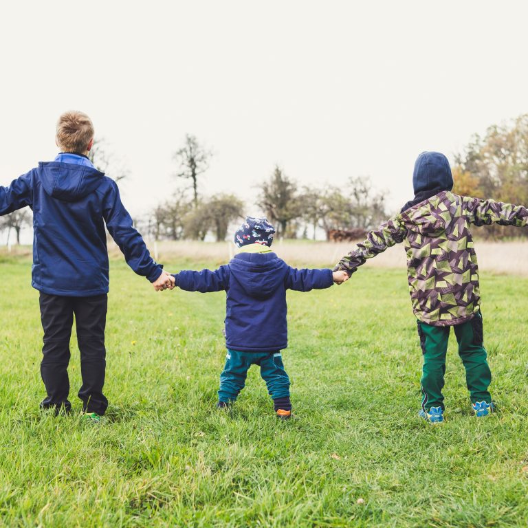 Kolme lasta pitelevät käsiä vihreällä niityllä.