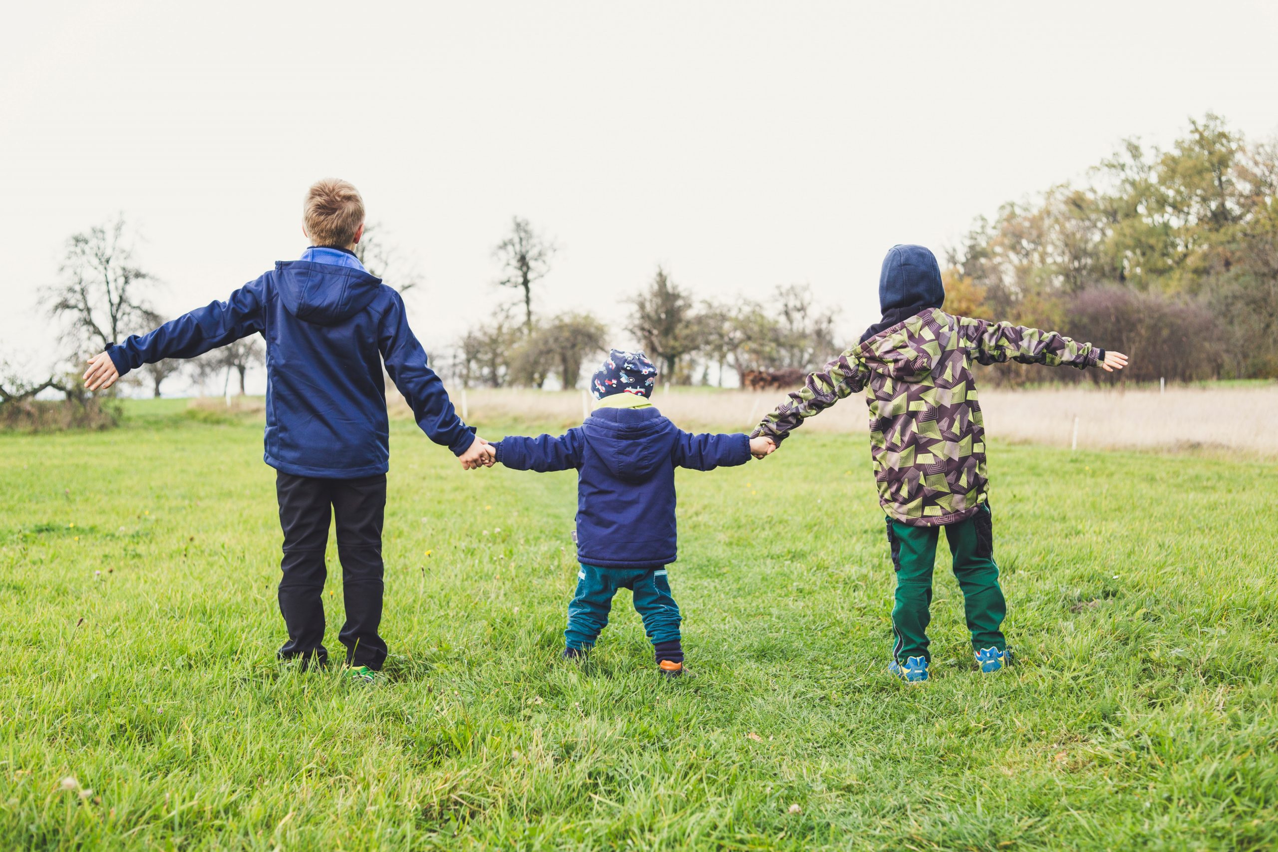 Kolme lasta pitelevät käsiä vihreällä niityllä.