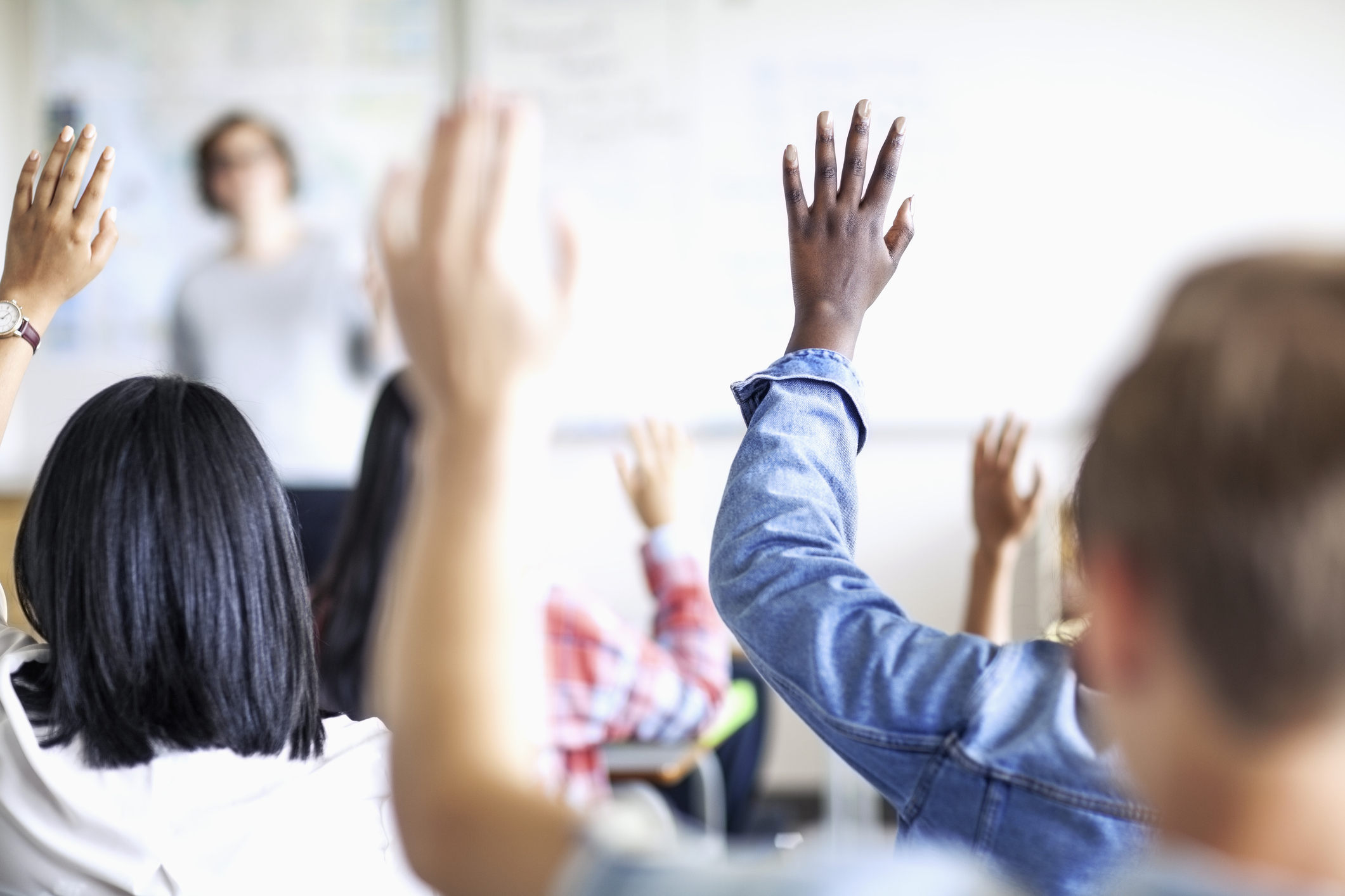Oppilaita käsi ylhäällä luokkahuoneessa.